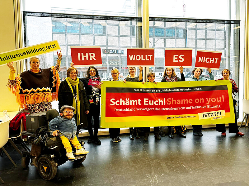 Wir prostestieren im Berliner Congress Centrum. Auf den Bannern steht "Schämt Euch", "Ihr wollt es nicht!" und "Inklusive Bildung Jetzt" - im Vordergrund sitzt Raul Krauthausen.