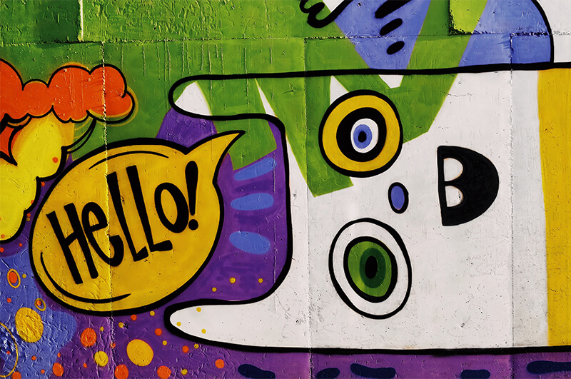 Ein Graffitikopf mit Sprechblase in der "Hello!" steht.